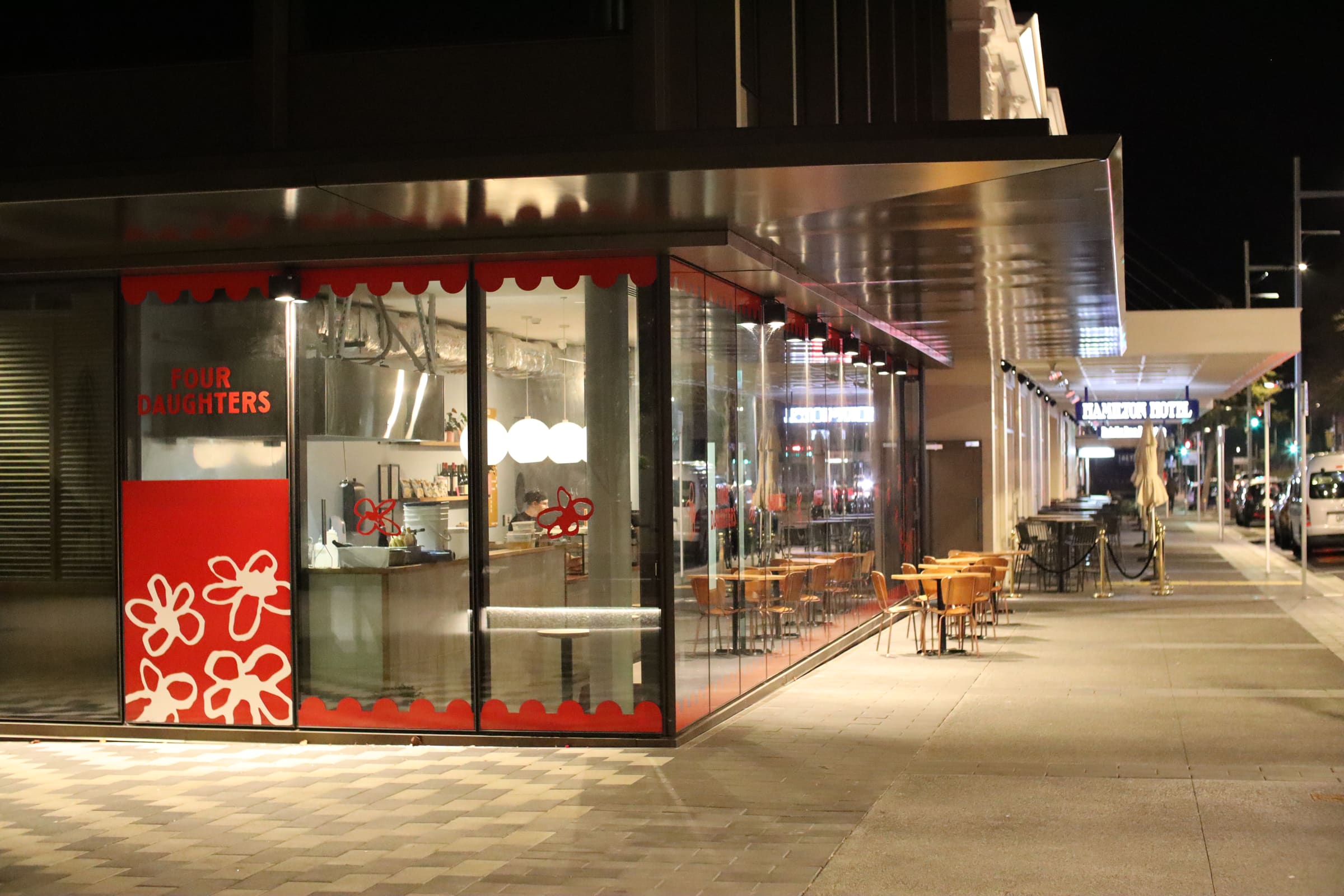 Illuminated glass-fronted exterior of Four Daughters restaurant at night